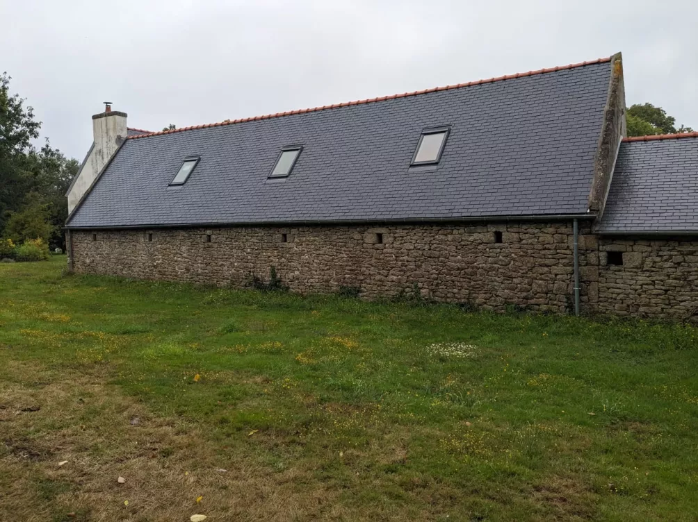 Façade d’une maison en pierres avec un toit à double pente, fenêtres de toit visibles.