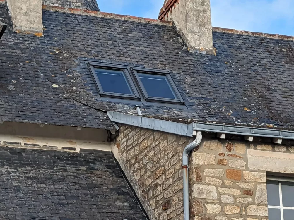 Détail de toit en ardoise avec fenêtres de toit et système de gouttières visibles.
